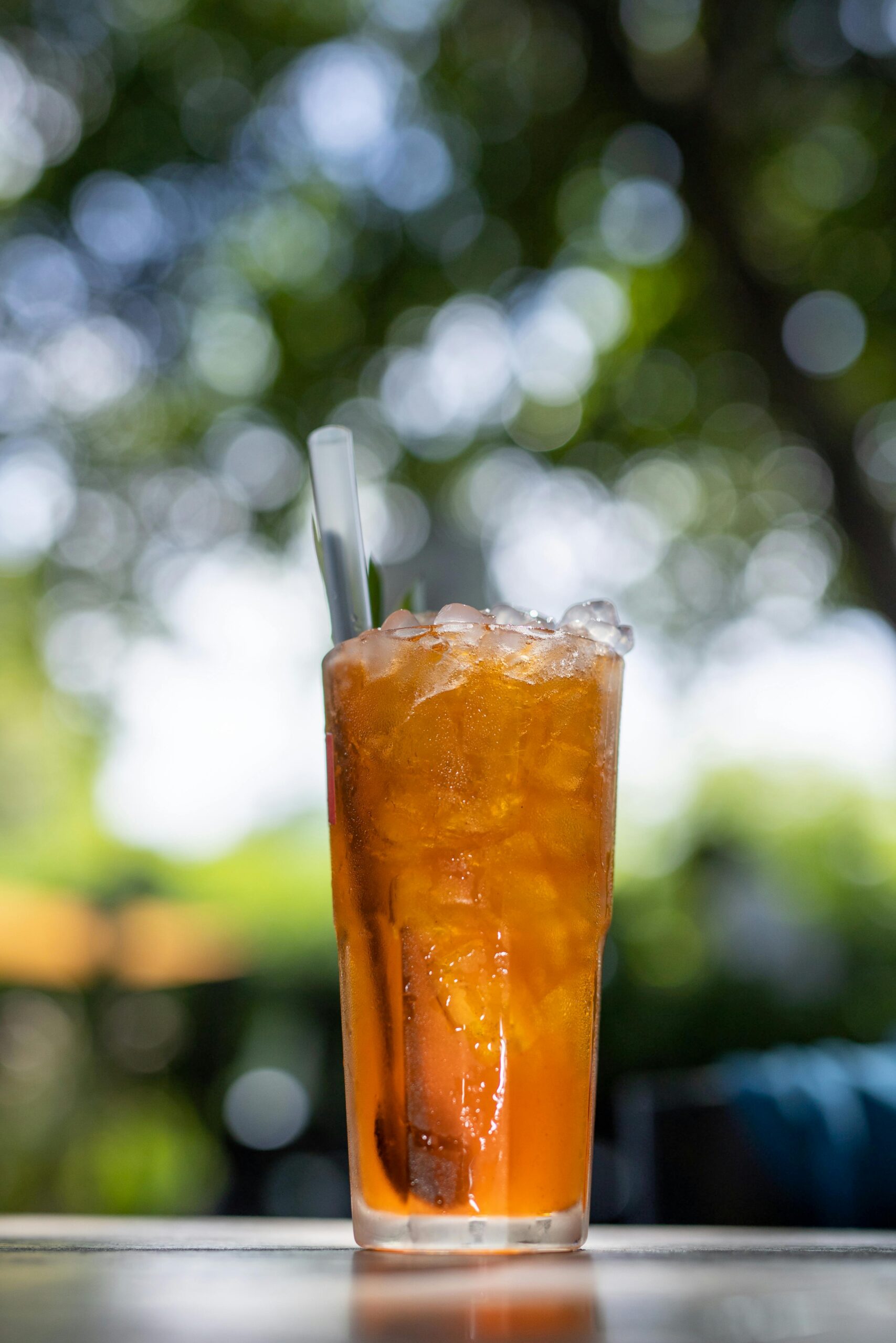 A refreshing glass of iced tea with a citrus twist, set outdoors with blurred natural background.